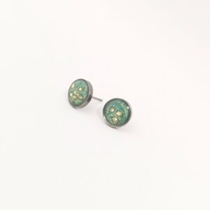 Three small round coins with green patina and gold flecks on a pale surface, arranged diagonally toward the bottom-left.