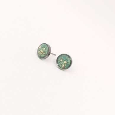 Three small round coins with green patina and gold flecks on a pale surface, arranged diagonally toward the bottom-left.