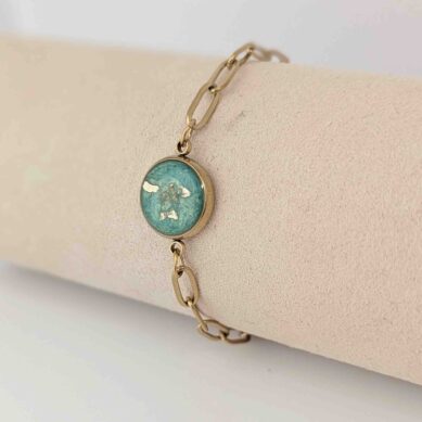 Gold chain necklace with an oval turquoise pendant resting on a beige surface