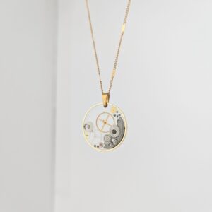 PXL_20261014_162222382 - Blue Pendulum Jewelries Gold pocket watch pendant hanging on a delicate gold chain against a pale background.