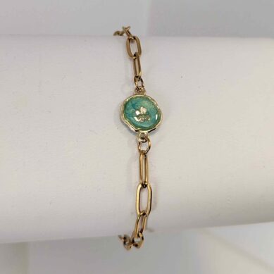 Gold chain necklace with an oval turquoise pendant hanging against a white background