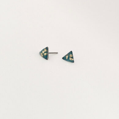 Pair of teal triangular stud earrings with gold leaf patterns resting on a pale surface, one facing up and one slightly tilted.