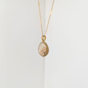 PXL_20261013_164117438 - Blue Pendulum Jewelries Gold chain necklace with a teardrop-shaped pink stone pendant hanging against a pale background, close-up view.