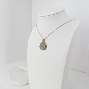 PXL_20261013_164430180 - Blue Pendulum Jewelries Gold chain necklace with an oval blue-green pendant displayed on a white jewelry bust.