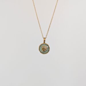 PXL_20261013_165036078PORTRAITORIGINAL - Blue Pendulum Jewelries Gold chain necklace with an oval pendant showing a bird illustration on a blue-green background