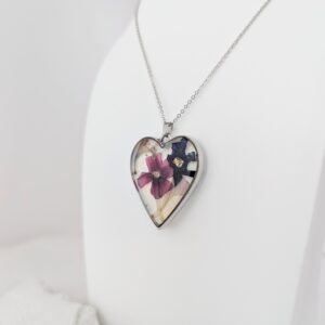 PXL_20261013_174310211 - Blue Pendulum Jewelries Heart-shaped pendant with a colorful abstract design on a silver chain, resting on a white surface.