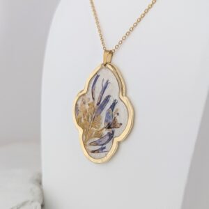 PXL_20261013_182345455PORTRAIT - Blue Pendulum Jewelries Gold chain with an oval pendant, containing pressed blue and yellow flowers encased in clear resin.