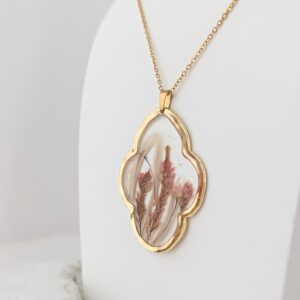 PXL_20261013_182806198PORTRAITORIGINAL - Blue Pendulum Jewelries Gold chain necklace with a teardrop-shaped pendant containing dried flowers on a white surface.