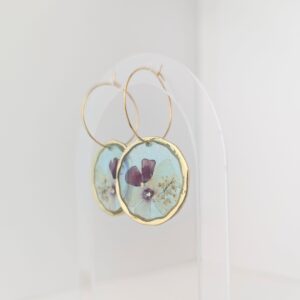 PXL_20261013_195619070 - Blue Pendulum Jewelries Decorative wall hanging with gold hoops and botanical prints against a pale background.
