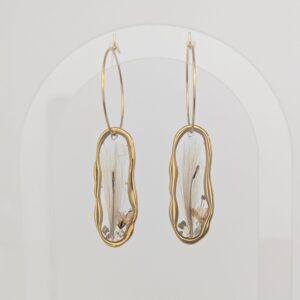 PXL_20261014_140711621PORTRAITORIGINAL - Blue Pendulum Jewelries Gold hoop earrings with oval glass pendants hanging against a pale background.