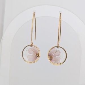 Gold hoop earrings with circular glass pendants containing pink floral designs on a white background.