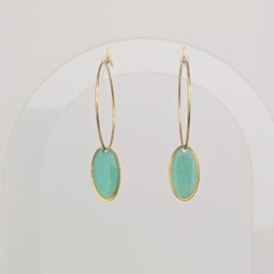 Gold hoop earrings with turquoise oval pendants hanging against a pale background, close-up view on a white surface.