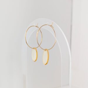 Gold hoop earrings displayed on a clear stand against a light background, product photography.